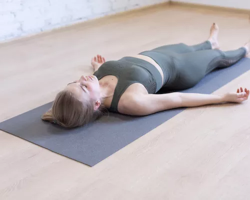 Une femme allongée sur un tapis de yoga pendant un cours de nidra yoga
